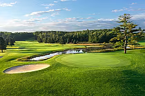 Scenic view of the Alpine Course at Boyne Mountain, featuring lush fairways, a sand trap, and a serene water hazard.