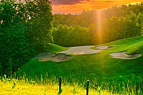 Sunset over lush golf course with vibrant green fairways, sand traps, and trees at Treetops in Michigan.