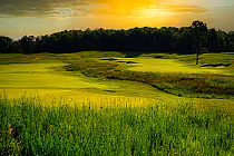 Sunset over Smith Tradition Golf Course at Treetops Resort, lush fairways with sand traps, surrounded by trees.