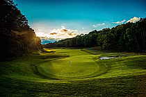 Scenic view of Fazio Premier Golf Course at sunrise, with lush greens, trees, and a vibrant sky at Treetops Resort, Michigan.