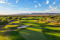 Scenic view of lush green golf course with sand trap, trees, and distant mountains at Whirlwind Golf Club, Arizona.