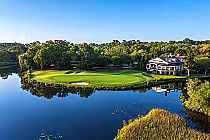 Aerial view of Caledonia Golf & Fish Club, showcasing lush greens, a reflective pond, and an Old South-style clubhouse.
