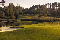 Golfers on a lush green course at Panther's Run, surrounded by trees and water, under a clear sky.