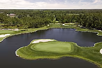 Aerial view of Tiger's Eye golf course, featuring a lush green island hole surrounded by clear water and tall green trees.