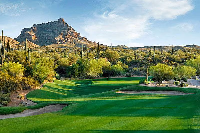 Scenic view of a golf course with lush green fairways, desert plants, and a mountain backdrop in Scottsdale, Arizona.