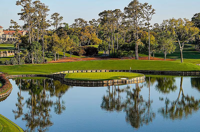Scenic view of a golf course at TPC Sawgrass with a green, water hazard, trees, and a clear sky in the background.