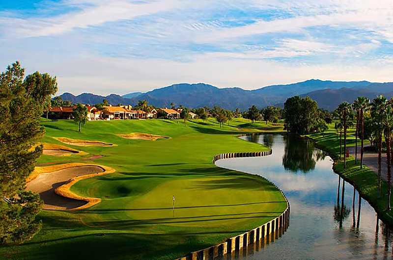 Scenic view of a golf course at Palm Springs with lush green fairways, sand traps, water hazards, palm trees, and mountains in the background.