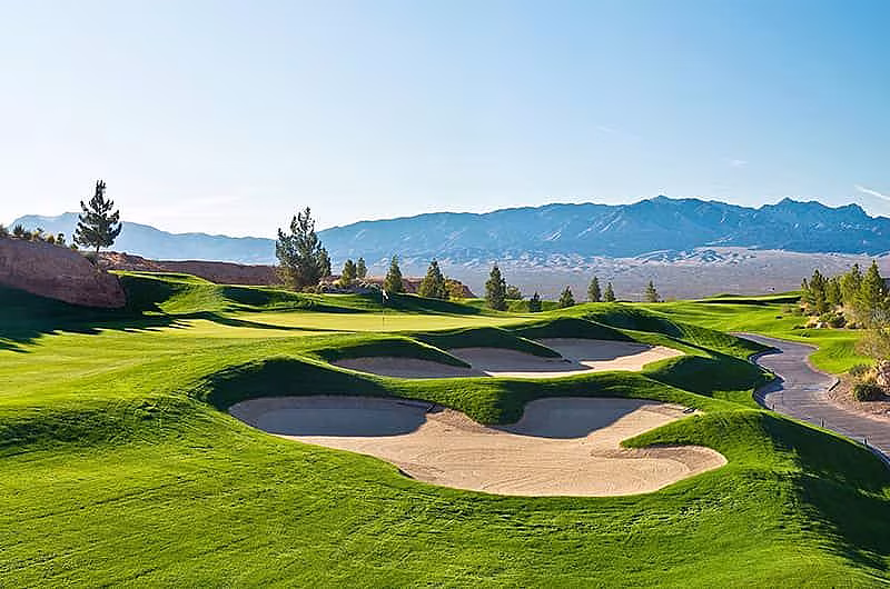 Beautiful view of a golf course with sand traps, lush green fairways, and distant mountains under a clear blue sky.