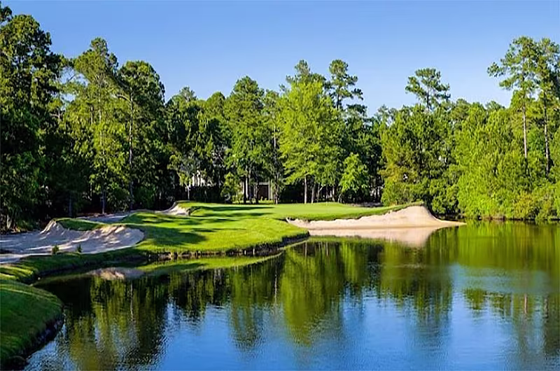 Beautiful golf course in Myrtle Beach with lush green fairways, sand traps, and water hazards, surrounded by tall trees and blue sky.