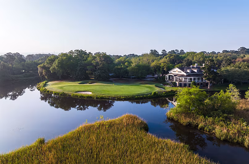 Scenic golf course in Myrtle Beach with a green, water hazard, trees, and a house in the background, perfect for a golf vacation.