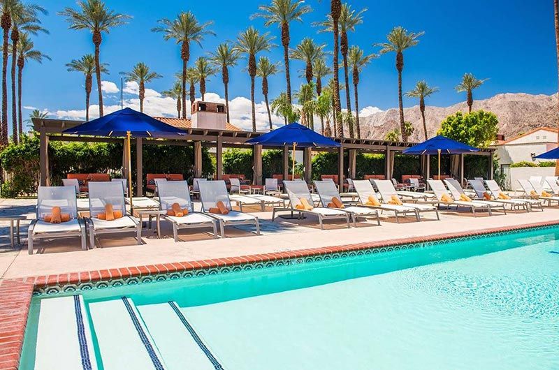 La Quinta Resort and Club Luxury poolside area at La Quinta Resort with lounge chairs, umbrellas, palm trees, and mountain backdrop.