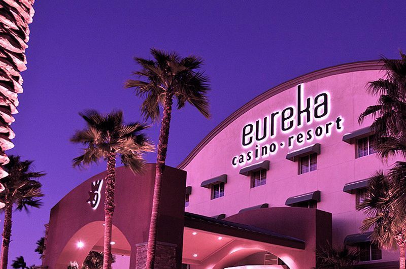 Eureka Casino Resort in Mesquite illuminated with pink and purple lights, featuring palm trees and a modern exterior at night.