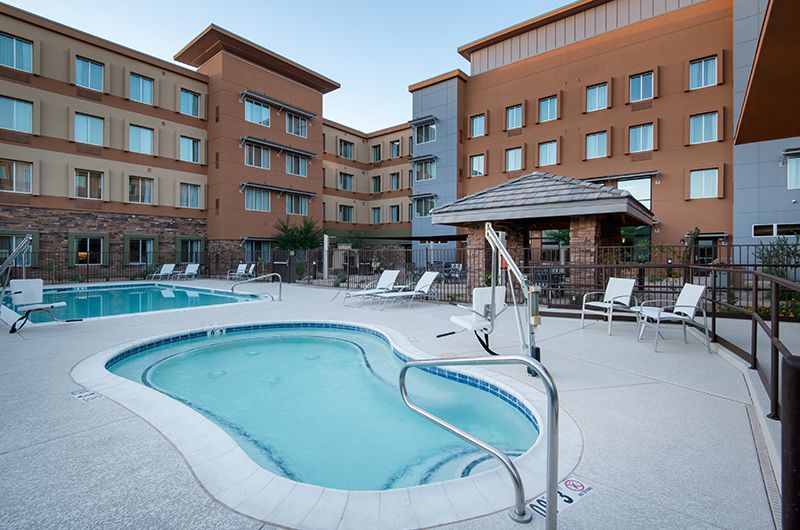 Outdoor pool and hot tub area at StayBridge Suites in Central Scottsdale, with lounge chairs and hotel building in background.