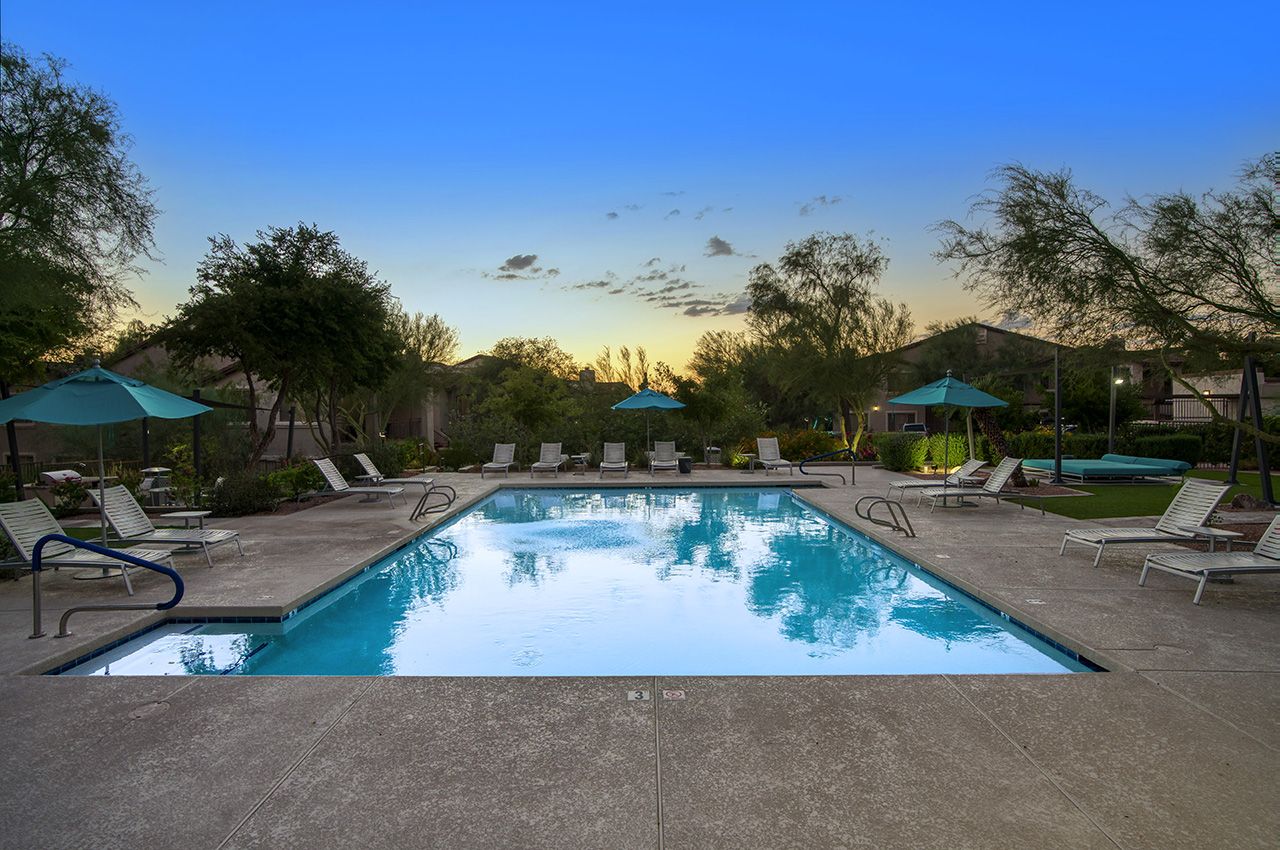 Luxury villas at McDowell Mountain Scottsdale with a swimming pool, lounge chairs, umbrellas, and lush greenery at sunset.