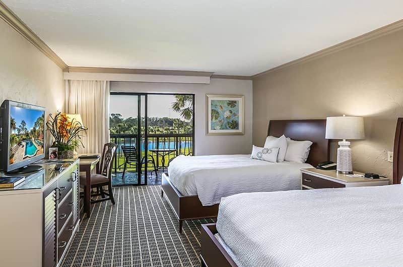 Interior of a hotel room at Mission Inn Resort & Club with two beds, a balcony view of lush greenery and a pool, and modern decor.