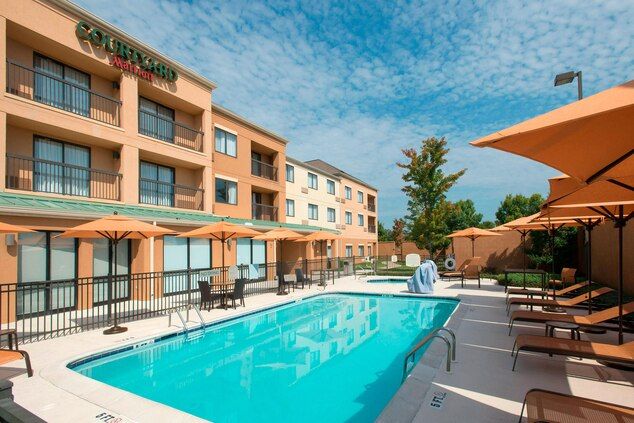 Pool area at Prattville Courtyard by Marriott with lounge chairs, umbrellas, and a hotel building in the background.