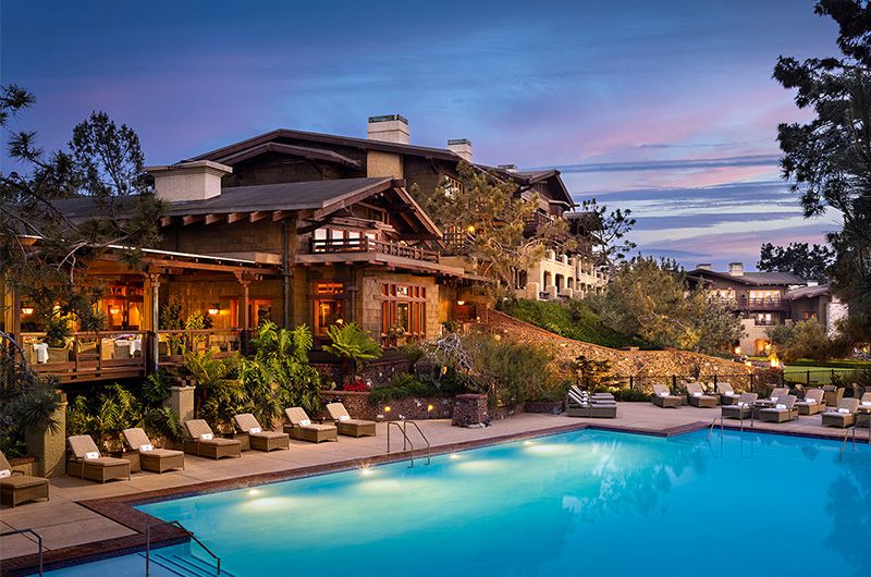 Luxury lodge with outdoor pool, lounge chairs, lush greenery, and scenic mountain views at sunset, perfect for a golf vacation.