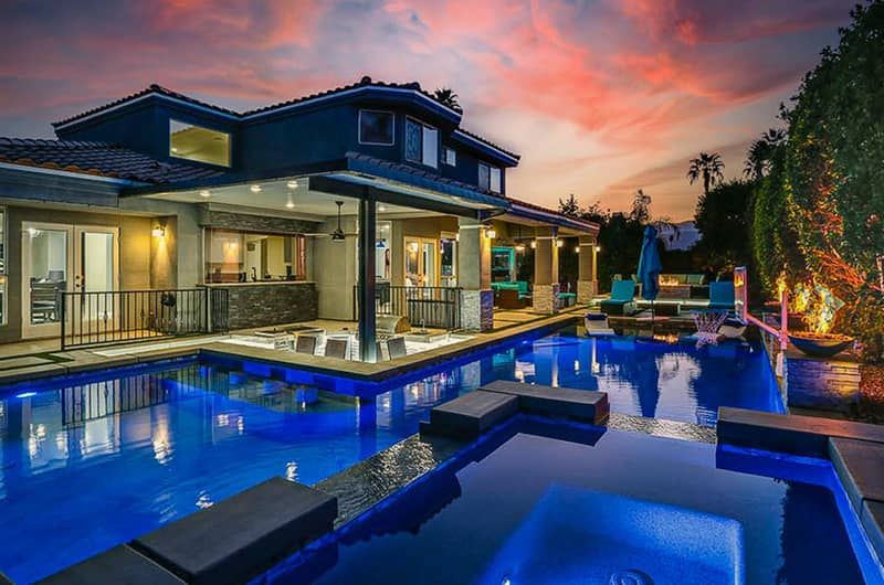 Hanging In Palm Desert Luxury backyard with a private pool, swim-up bar, outdoor seating, and a two-story house in Palm Desert at sunset.