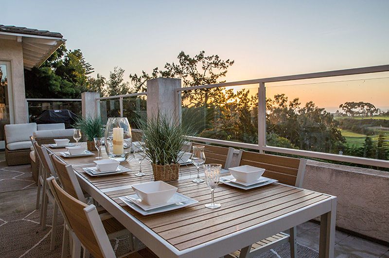 Elegant outdoor dining table set on a balcony with ocean and golf course views at sunset, perfect for luxury golf vacations.