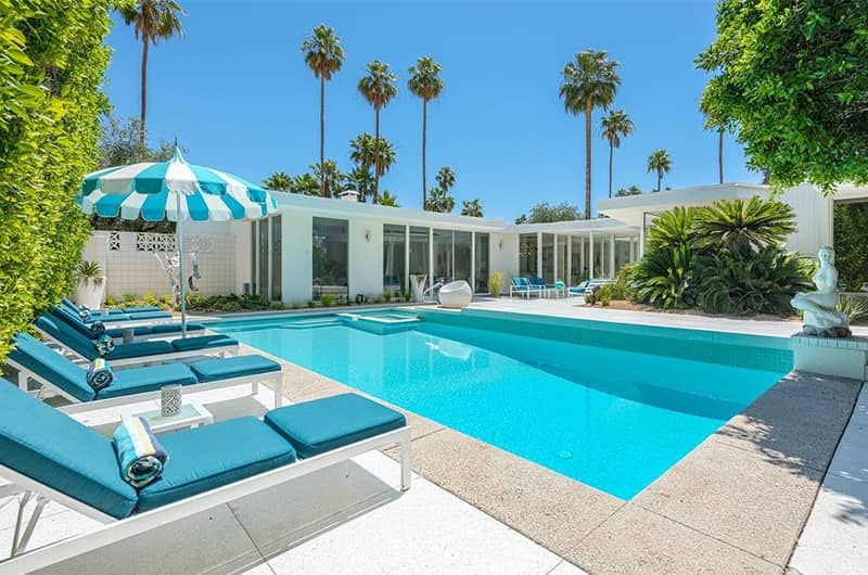 The Schwartz House Modern mid-century house with a private pool, spa, lush greenery, and tall palm trees under a clear blue sky.