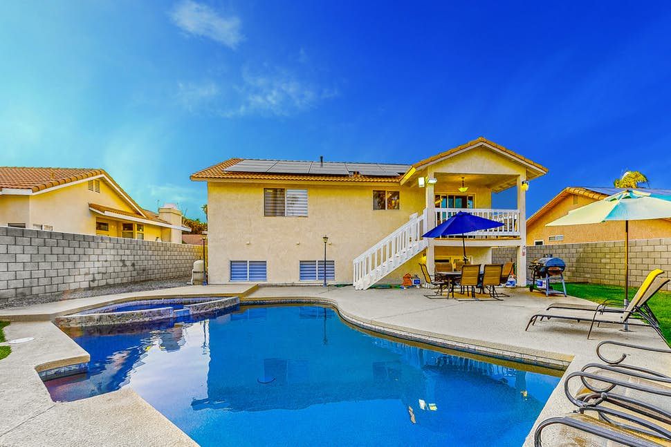Desert Breeze Sunny backyard with a swimming pool, patio furniture, umbrellas, and a two-story house with solar panels in Cathedral City.
