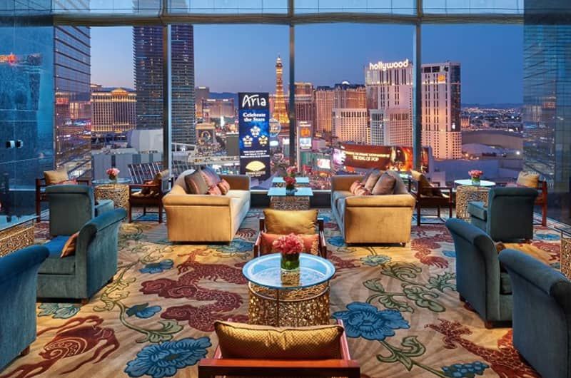 Waldorf Astoria Las Vegas Luxurious lounge with plush sofas, colorful cushions, and a floral rug overlooking Las Vegas skyline through large windows.