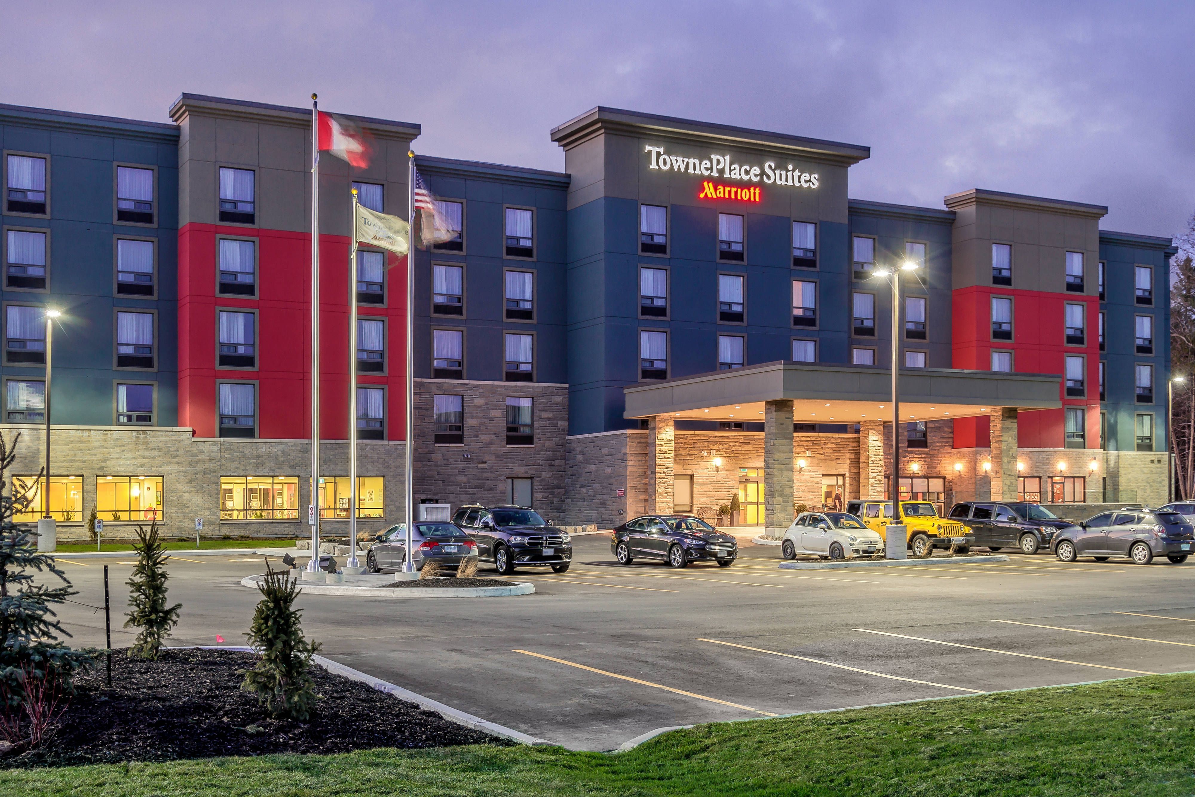 TownPlace Suites Belleville Exterior view of TownePlace Suites Belleville hotel at dusk, with parking lot, cars, flags, and illuminated signage.
