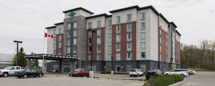 Homewood Suites Ajax Exterior view of Homewood Suites Ajax hotel with parking lot, Canadian flags, and a multi-story building near Highway 401.