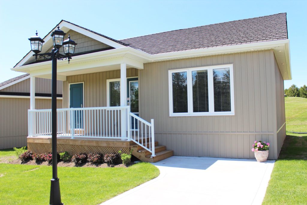 Royal Ashburn Cabins Modern beige cabin with white railing, large windows, and a small porch, set in a lush green landscape near a golf course.
