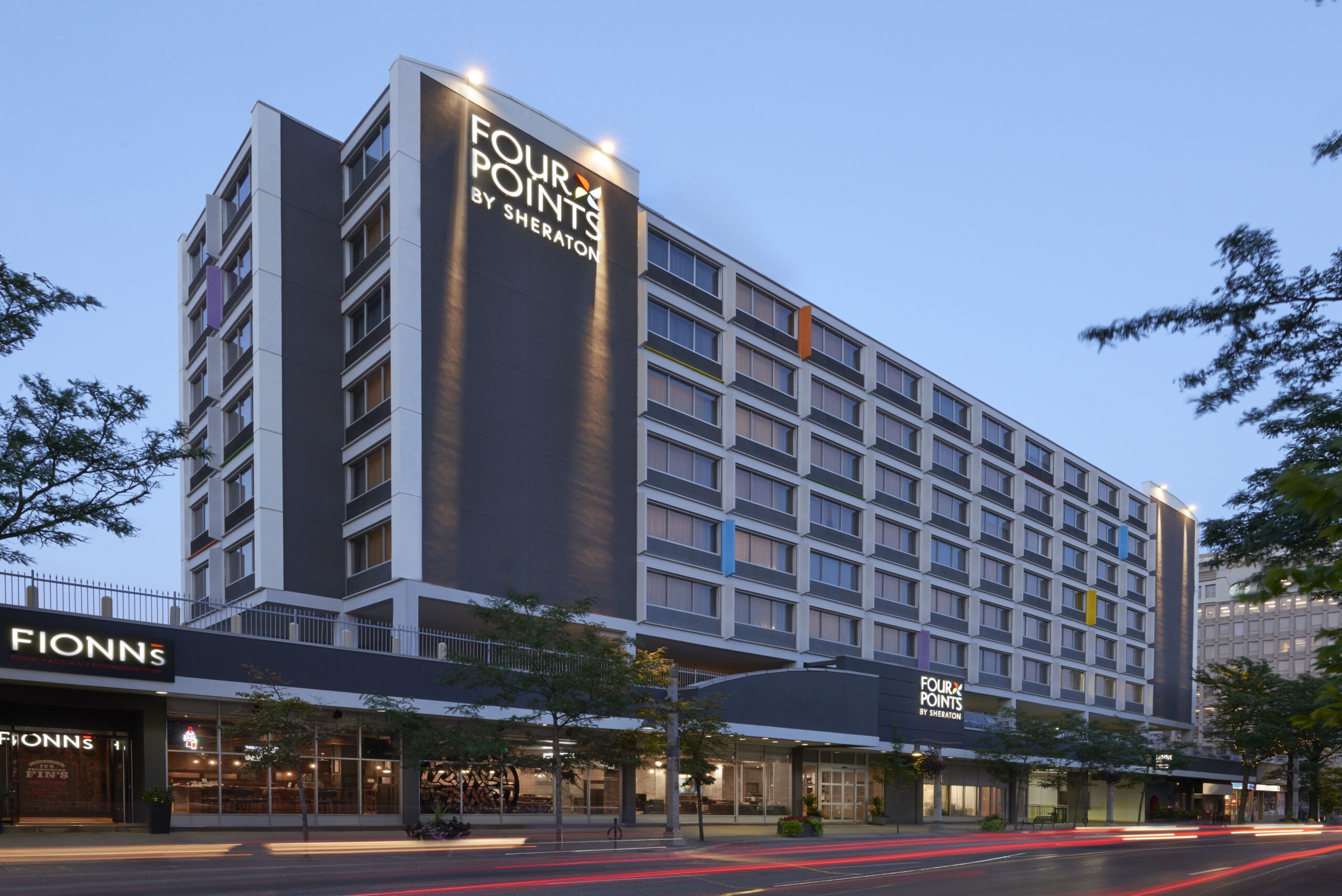Four Points Windsor Downtown - Parking Included Modern Four Points Windsor Downtown hotel building with illuminated signage, large windows, and a street view at dusk.