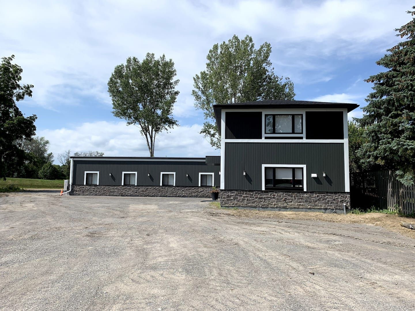 Dormie House / The Big House @Bay of Quinte G&CC Dormie House at Bay of Quinte G&CC, a modern luxury golf accommodation with black and white exterior, set against a blue sky and trees.