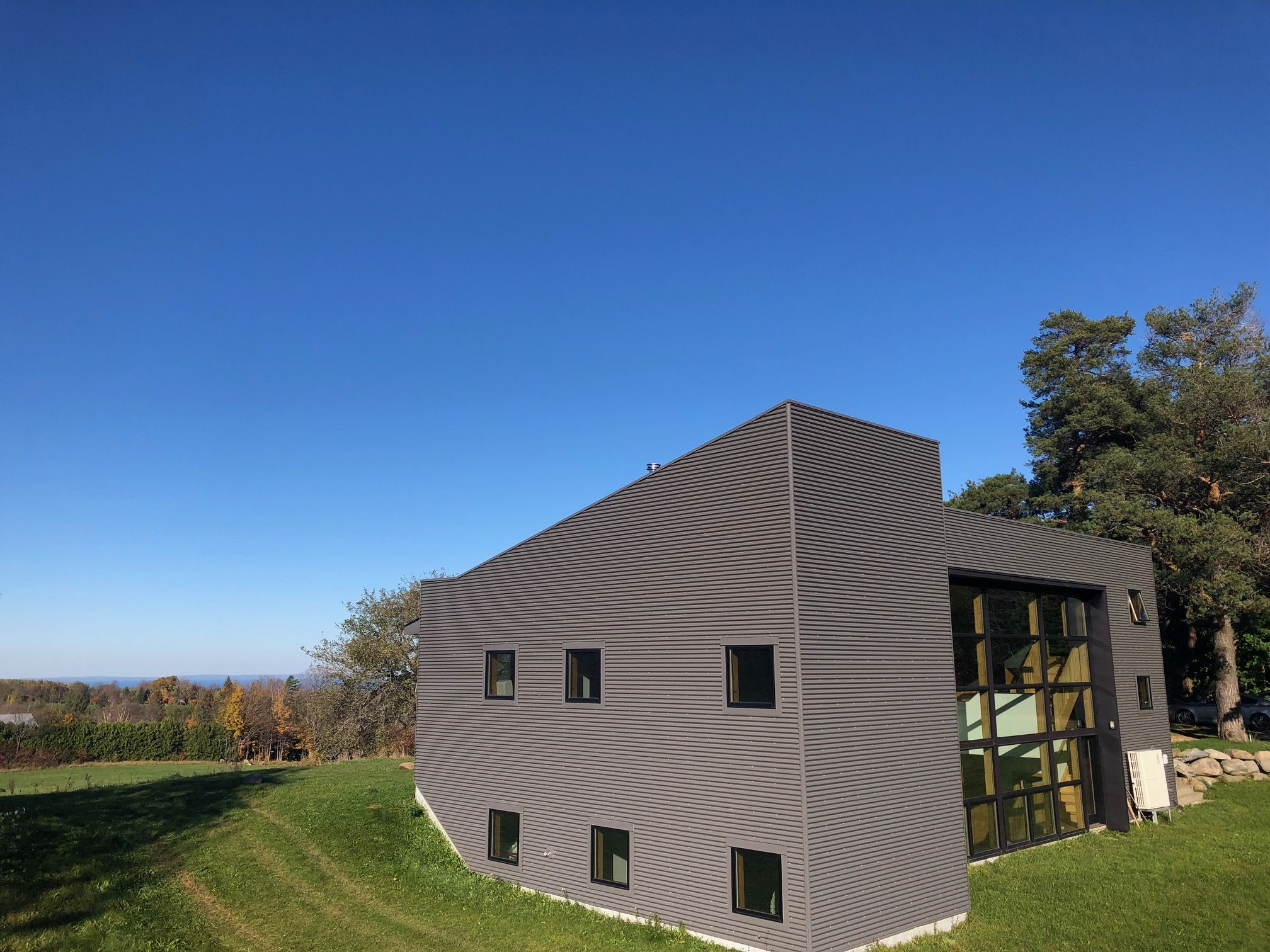 Highlands House Modern black building with large glass windows, set in a lush green landscape under a clear blue sky at Highlands House, Duntroon.