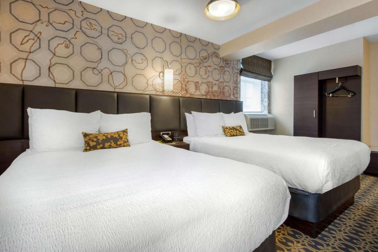 The Champlain Waterfront Hotel Interior of a modern hotel room with two large beds, white bedding, decorative pillows, a window with an air conditioner, and a closet.