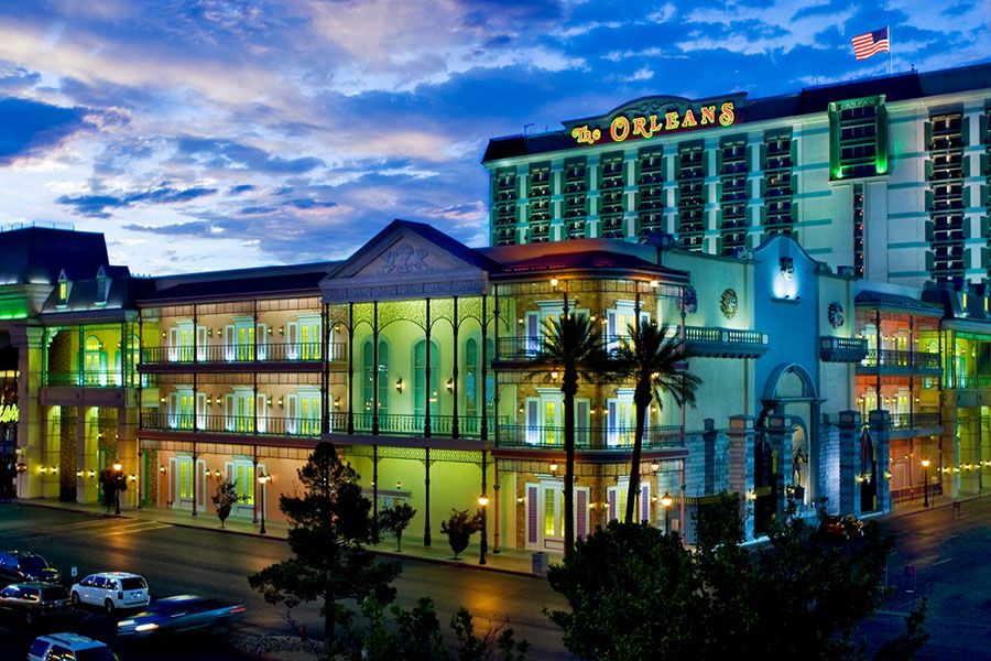 The Orleans Hotel & Casino Colorful illuminated Orleans Hotel & Casino in Las Vegas at dusk with a vibrant sky, palm trees, and parked cars in front.