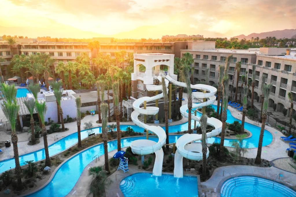 Grand Hyatt Indian Wells Resort & Spa Luxury resort pool area with water slides, palm trees, and sun setting in the background at Hyatt Regency Indian Wells.