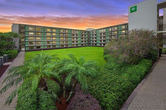 View of Wyndham Garden Lake Buena Vista Disney Springs Resort with lush greenery, palm trees, and a colorful sunset sky.