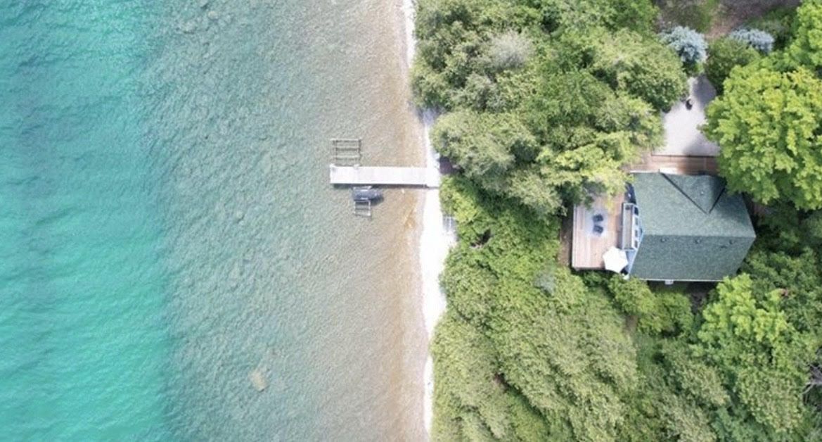 Brushview House A house with a deck by a clear, turquoise lake surrounded by lush green trees in Ontario, ideal for relaxing golf vacations.