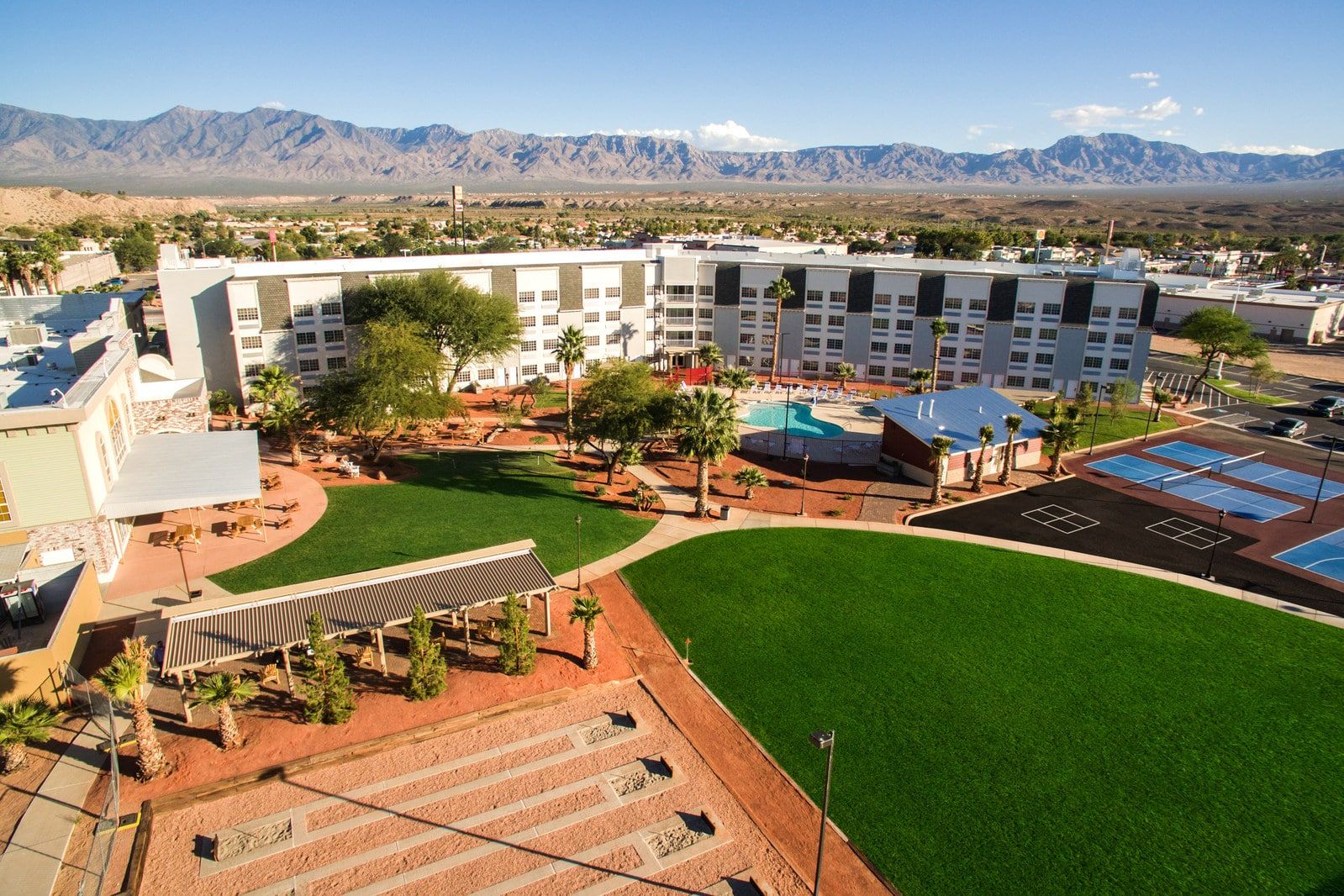 Aerial view of Rising Star Sports Ranch Resort in Mesquite, Nevada, featuring lush green lawns, swimming pool, tennis courts, and mountain backdrop.