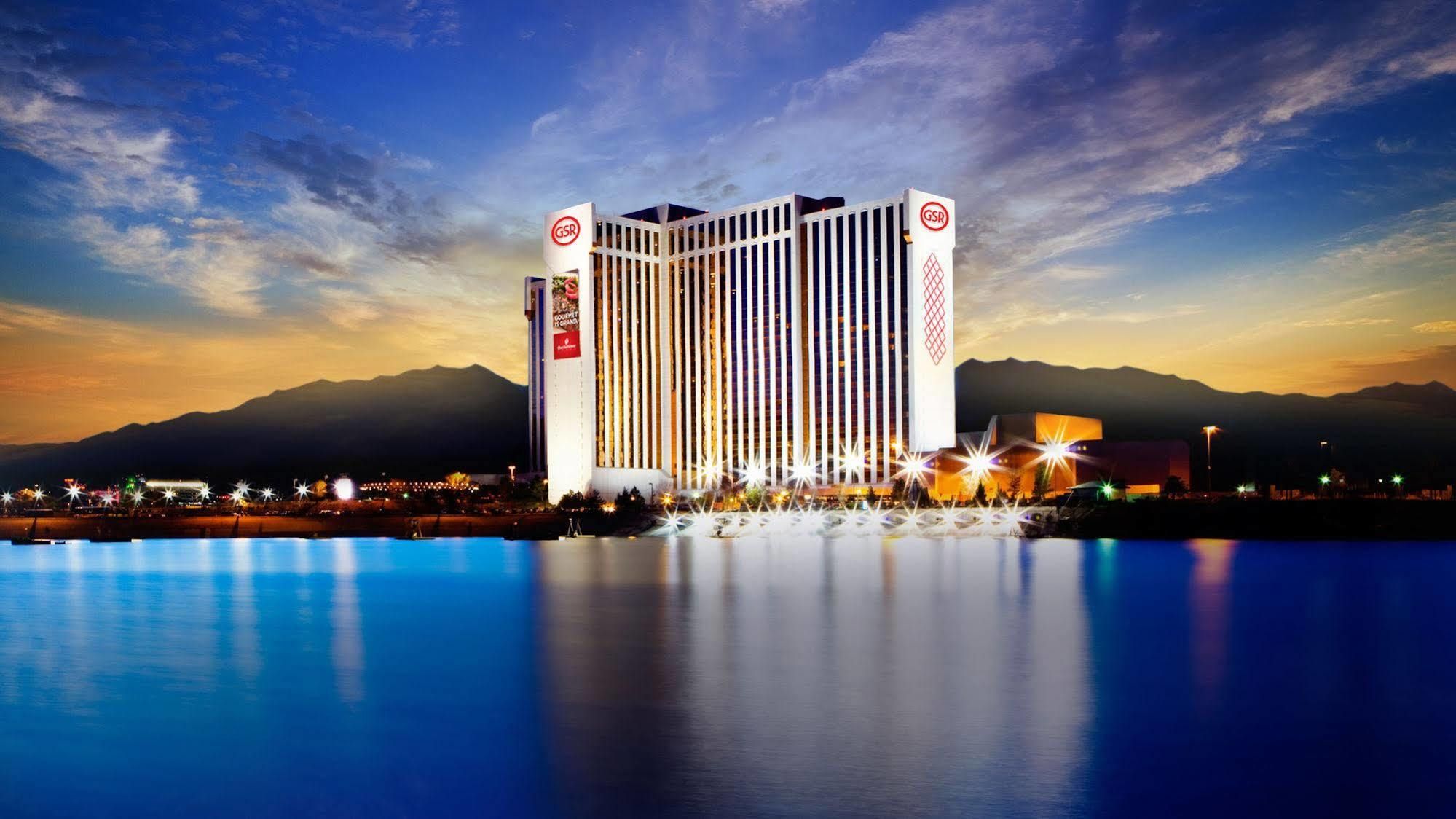 Grand Sierra Resort and Casino building illuminated at sunset with mountains in the background and a reflecting pool in the foreground.