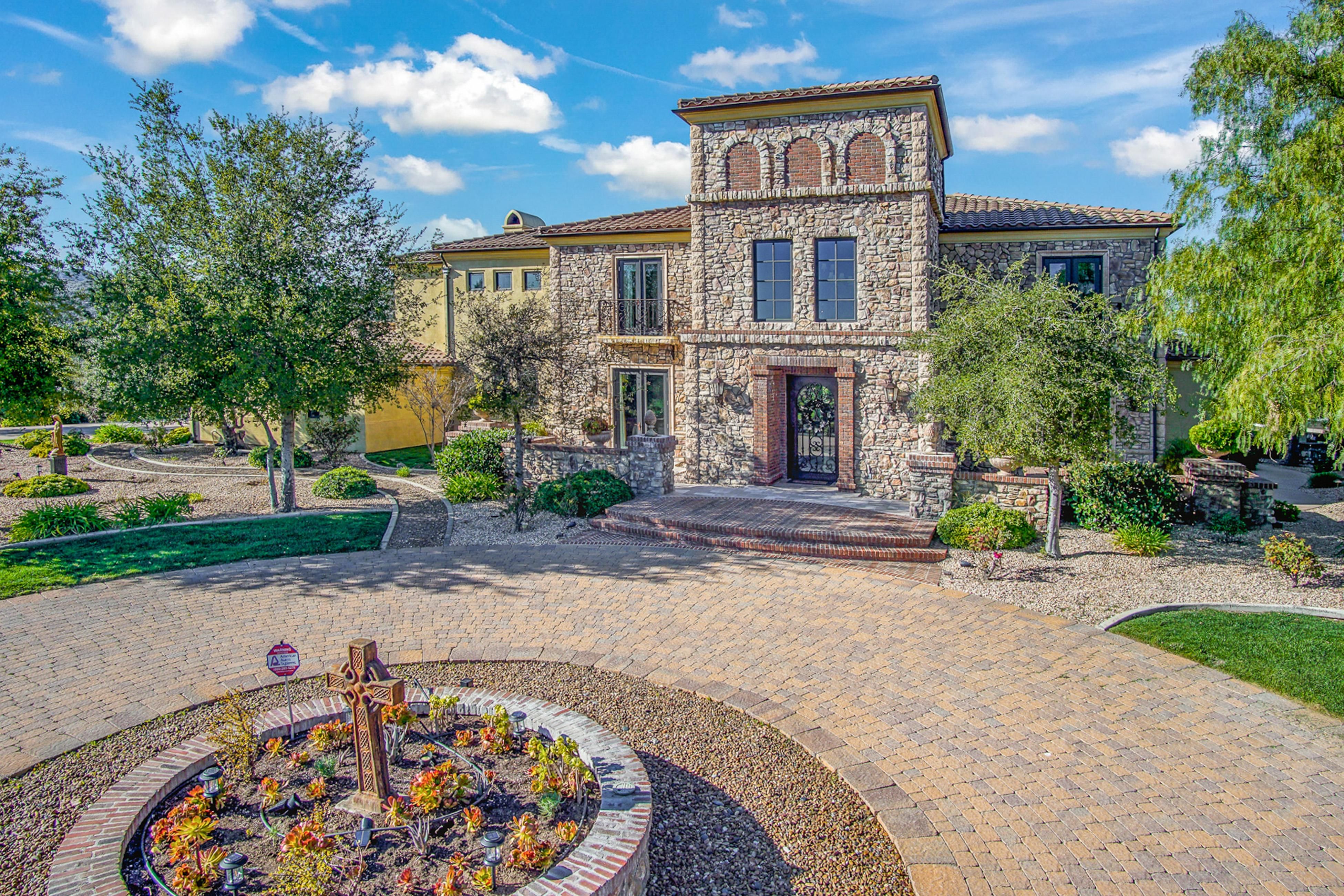 Luxury stone villa with landscaped garden, trees, and a circular brick driveway in a serene wine country setting.