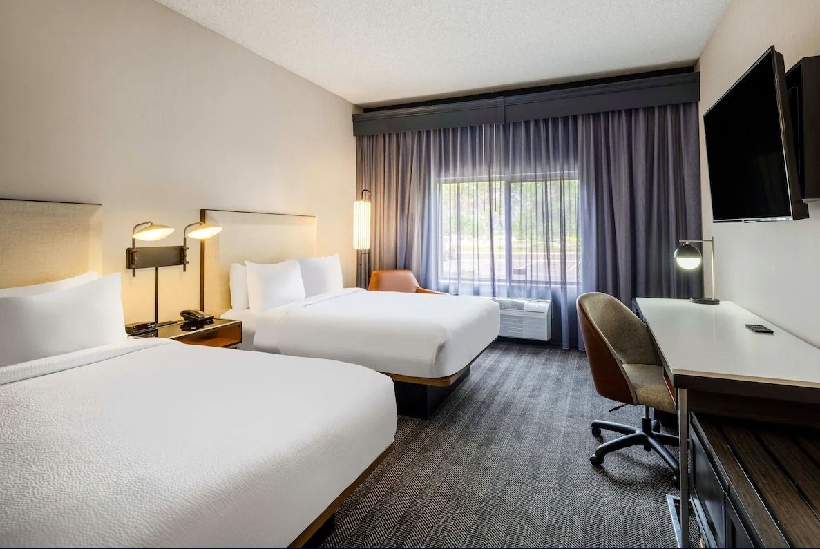 Modern hotel room at Courtyard Denver Southwest with two beds, desk, TV, large window, and cozy seating area.
