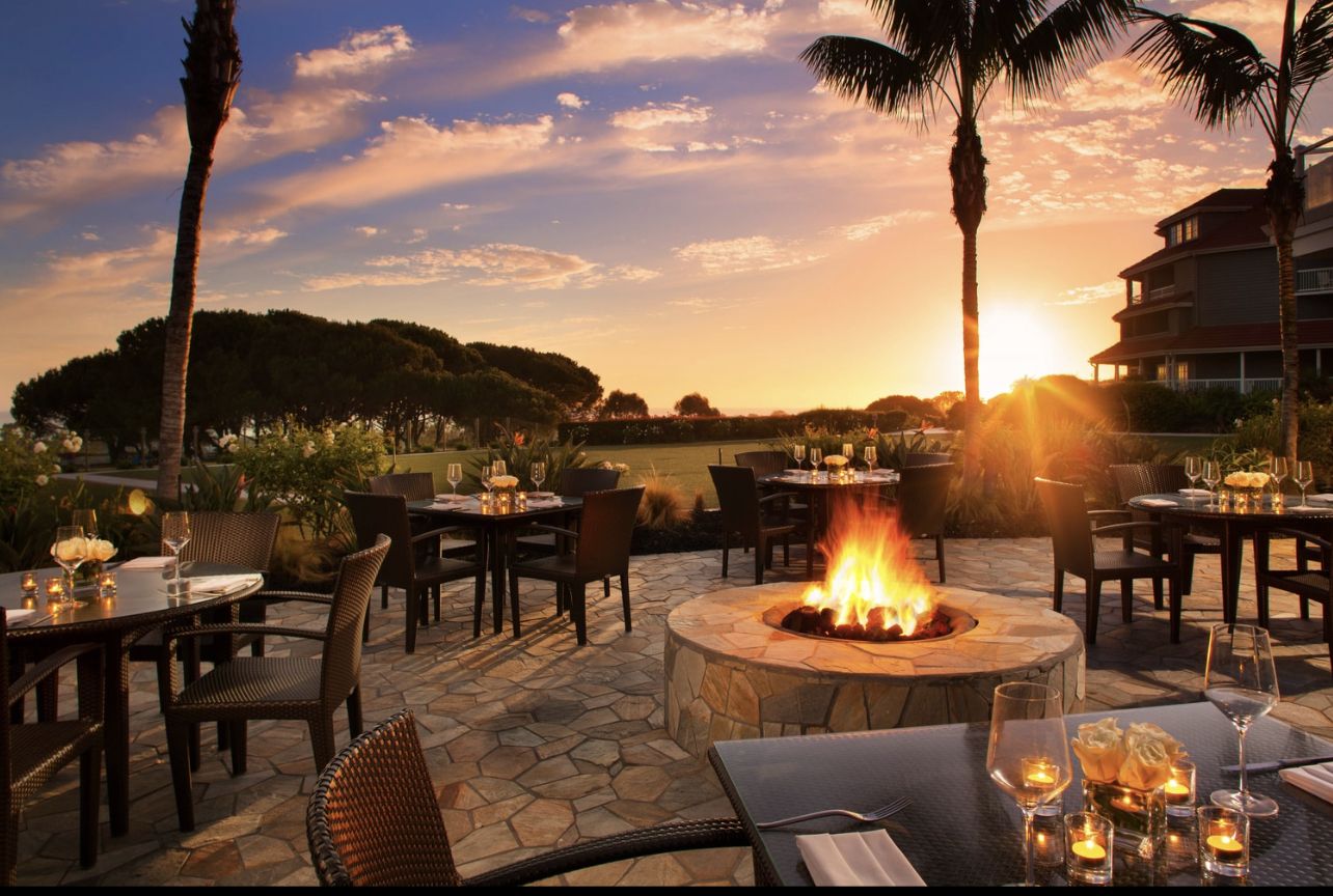 Outdoor dining area at Laguna Cliffs Marriott Resort & Spa with a fire pit, sunset, ocean views, and elegant table settings.