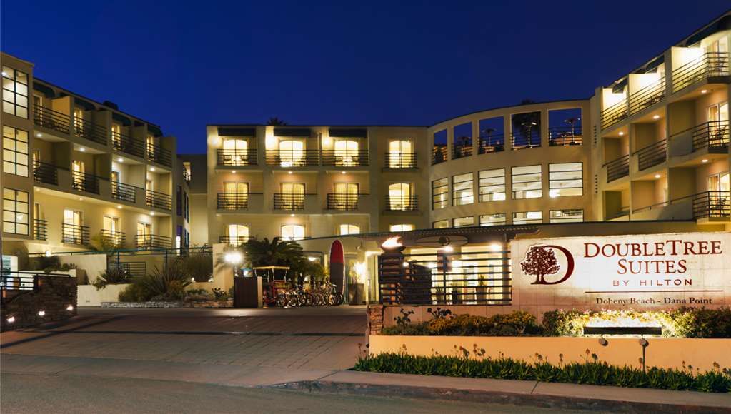 Night view of DoubleTree Suites by Hilton hotel at Doheny Beach, with illuminated windows and a sign in the foreground.
