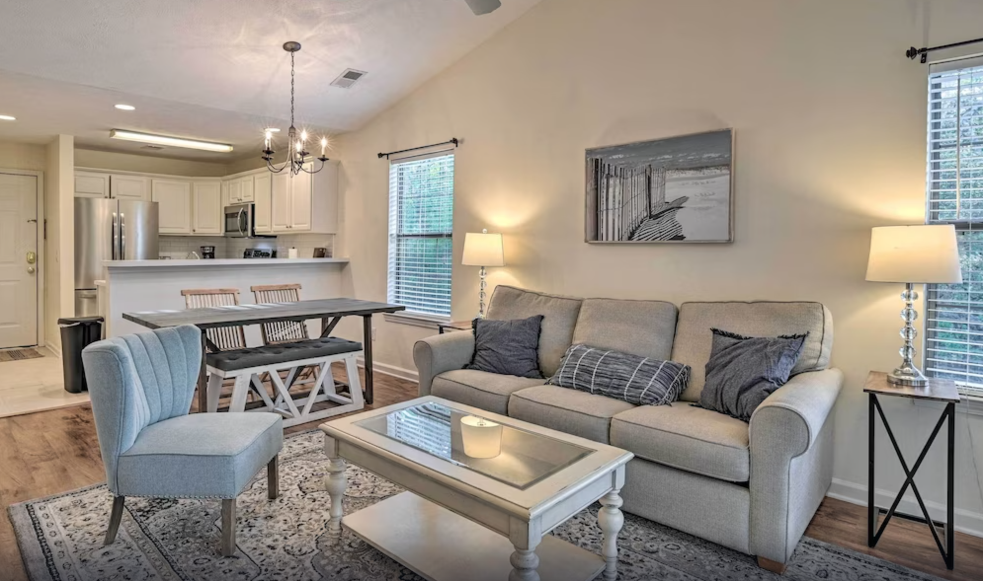 True Blue Golf Villas Interior of a cozy living room with a beige sofa, armchair, coffee table, and a view of the kitchen in a vacation villa.