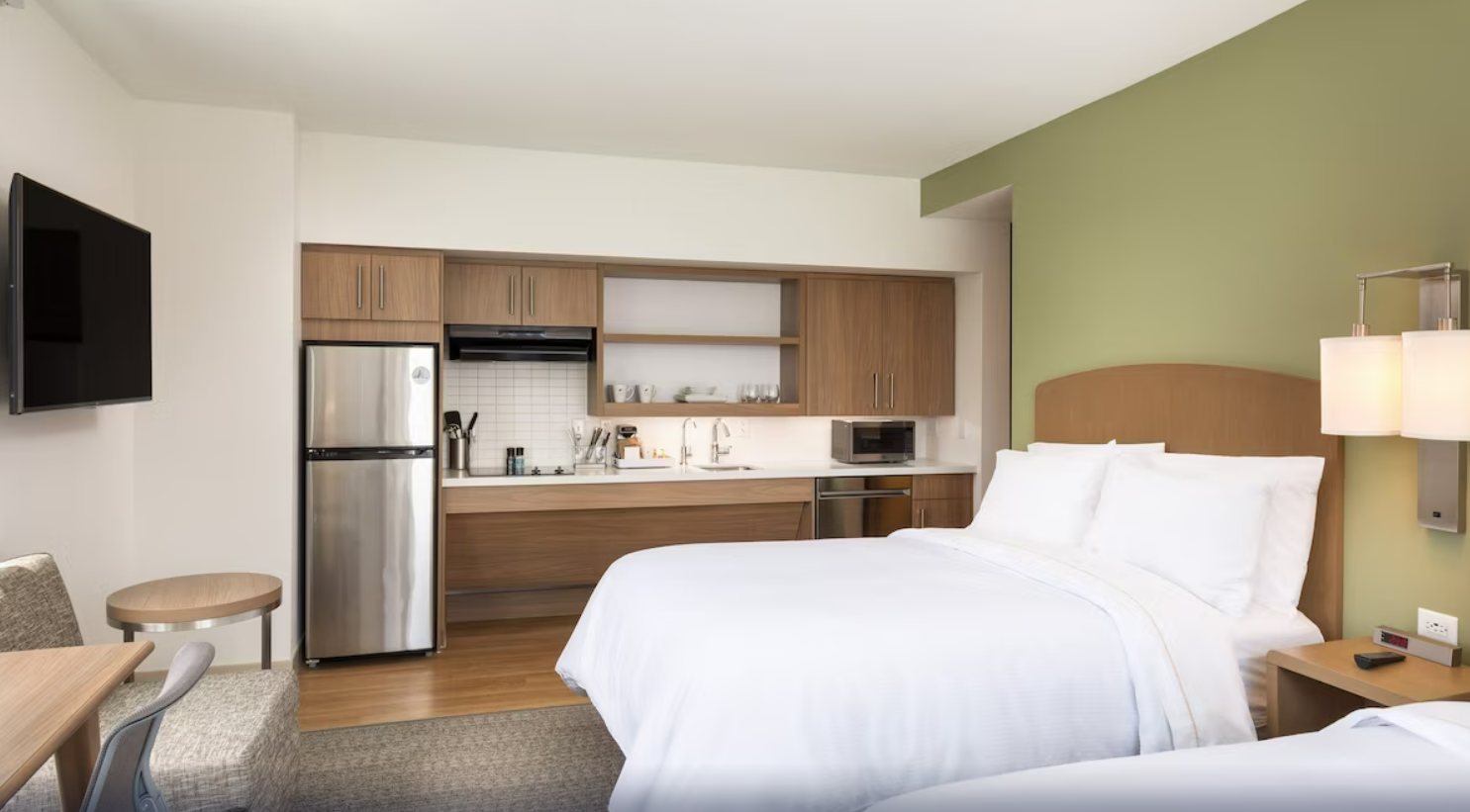 Interior of a modern hotel room with a bed, kitchenette, microwave, and a green accent wall, in Denver's Civic Center area.