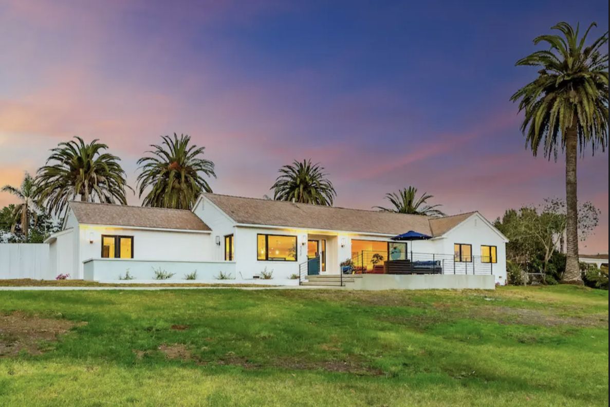Luxury vacation home in Carlsbad, CA with a pool, outdoor sitting area, firepit, surrounded by palm trees at sunset.