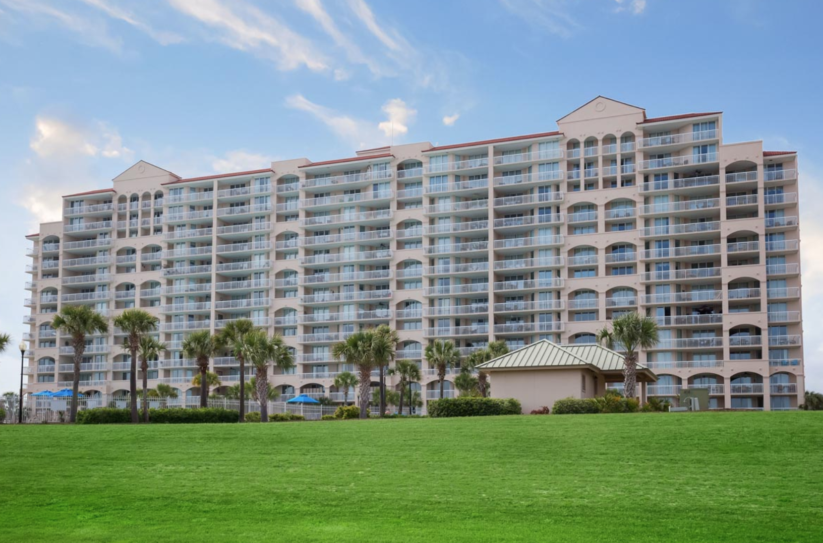 Barefoot Resort Yacht Club Luxury beachfront condo building with multiple balconies, surrounded by palm trees and lush green lawn under a blue sky.