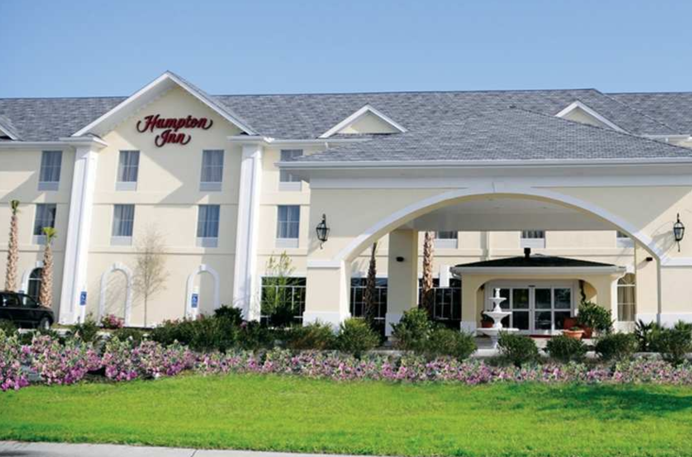 Hampton Inn Murrells Inlet Exterior view of Hampton Inn Murrells Inlet with a white facade, arched entrance, landscaped garden, and clear blue sky.