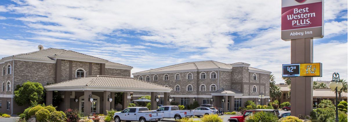 Exterior view of La Quinta Inn & Suites in St. George, a modern hotel with a stone facade, parking lot, and partly cloudy sky.