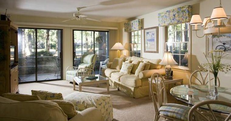 Pawleys Plantation Golf Villa Interior of a cozy, well-lit living room with beige sofas, floral curtains, and large windows overlooking a golf course in Myrtle Beach.